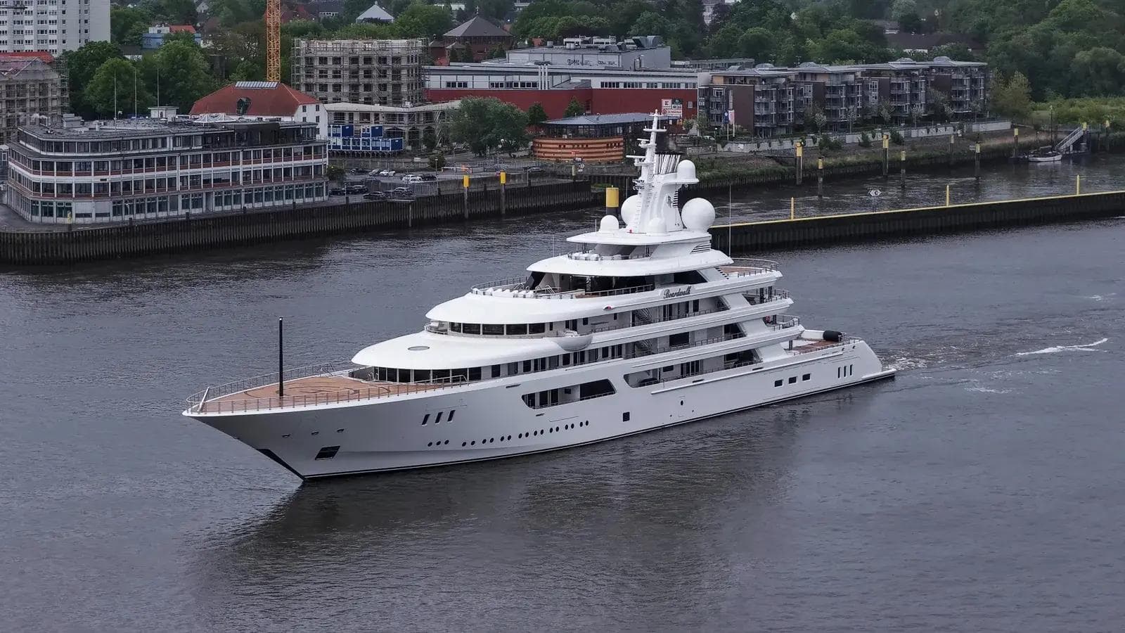 117m Lürssen superyacht Boardwalk in delivery transit, classical sheer line and proportional volume against industrial harbor backdrop
