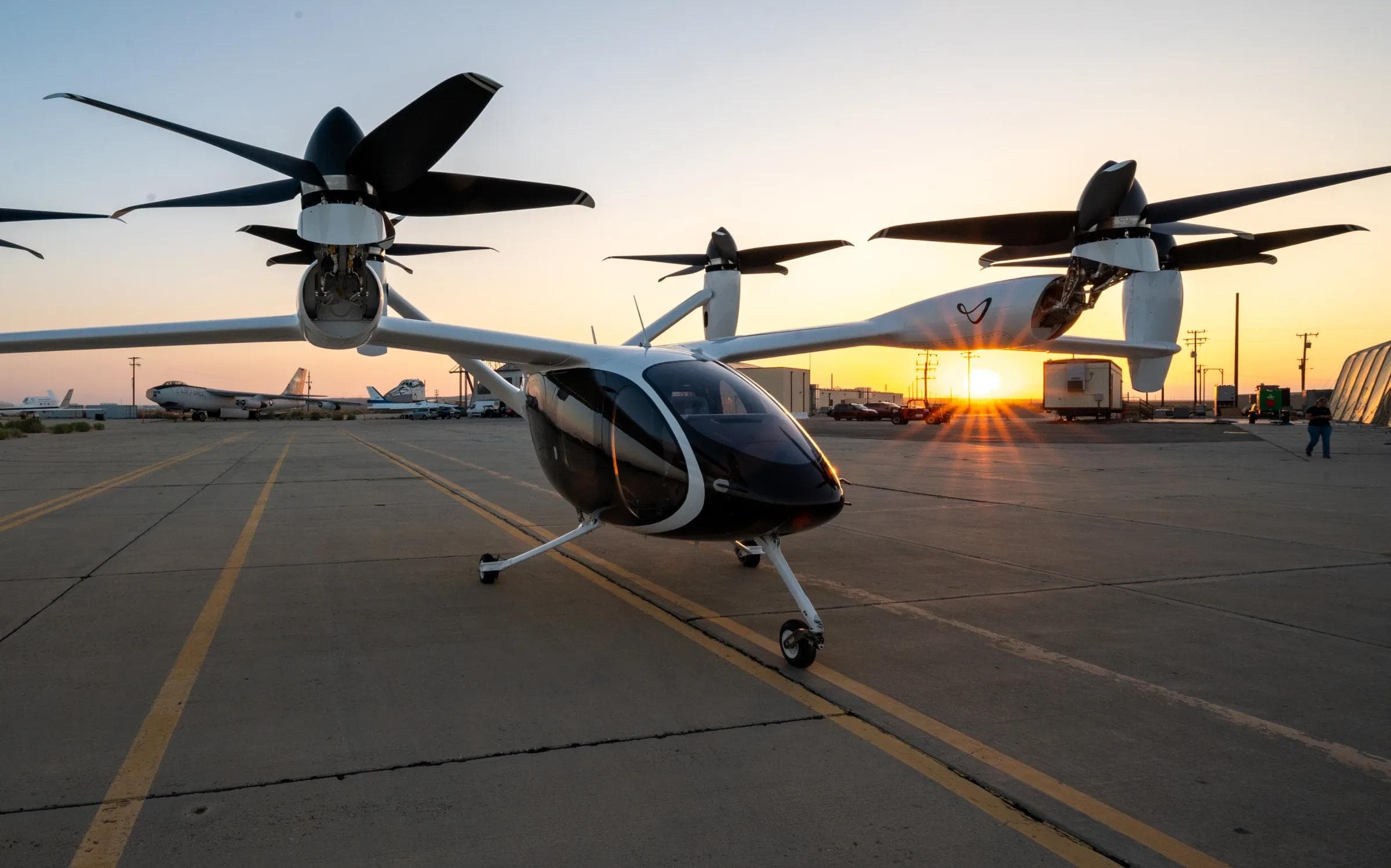 Joby S4 eVTOL aircraft on the tarmac at Edwards Air Force Base at golden hour, six tilting rotors prominent against a warm sunset sky