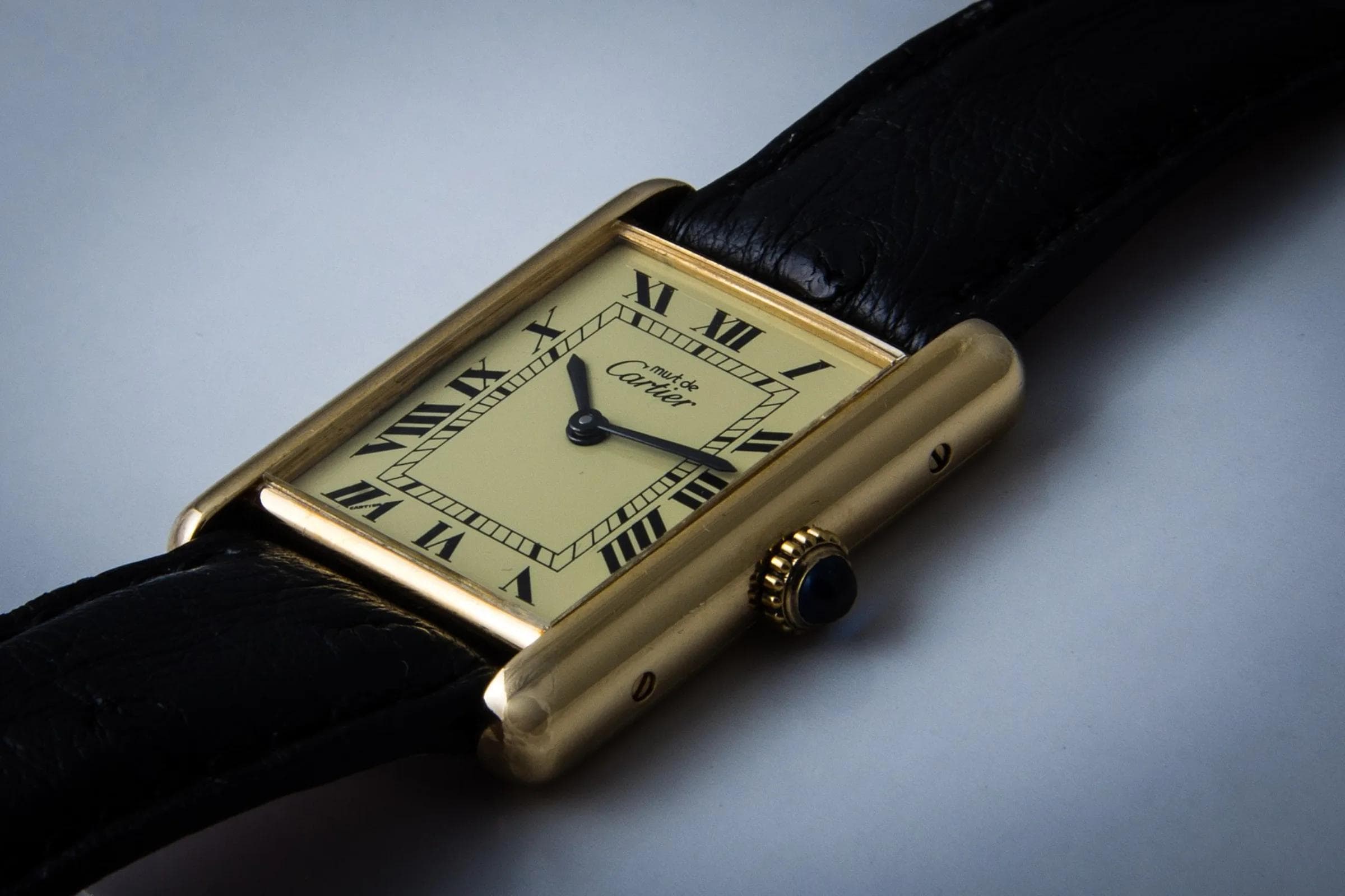 A yellow-gold Cartier Tank wristwatch with a cream Roman-numeral dial on a black leather strap